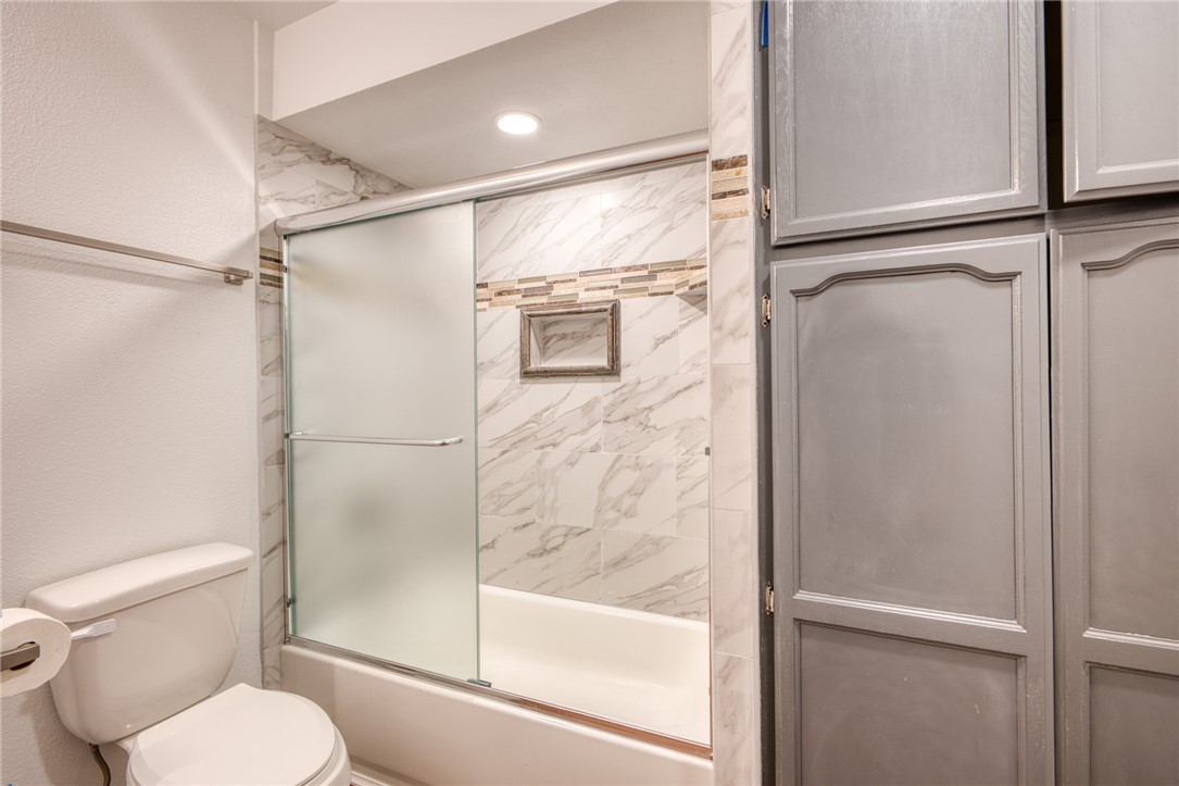 2053 Regents Road Mohave Valley, AZ 86440 - Photo 23 of 65 Bathroom featuring a white toilet, a bathtub with sliding frosted glass doors, and a tiled shower surround with a decorative accent band and niche