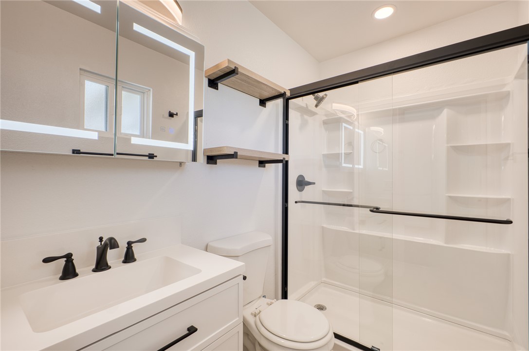 2053 Regents Road Mohave Valley, AZ 86440 - Photo 29 of 65 Bathroom featuring a vanity with an integrated sink and matte black faucet, an illuminated mirrored medicine cabinet, a toilet, and a shower with a sliding glass door