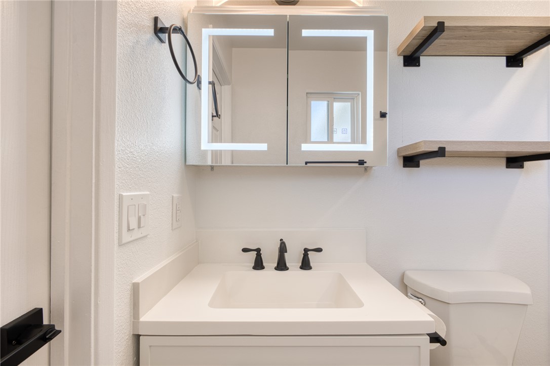 2053 Regents Road Mohave Valley, AZ 86440 - Photo 30 of 65 Bathroom featuring a vanity with a white countertop and dark fixtures, an illuminated mirrored medicine cabinet, and open shelving with dark brackets