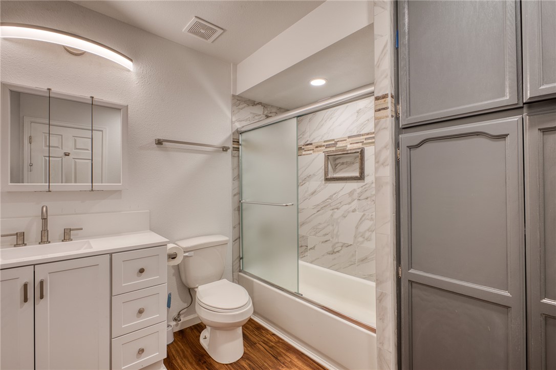 2053 Regents Road Mohave Valley, AZ 86440 - Photo 36 of 65 This bathroom features a white vanity with an integrated sink and brushed nickel fixtures, a toilet, and a bathtub with a sliding glass door and marble-style tile surround