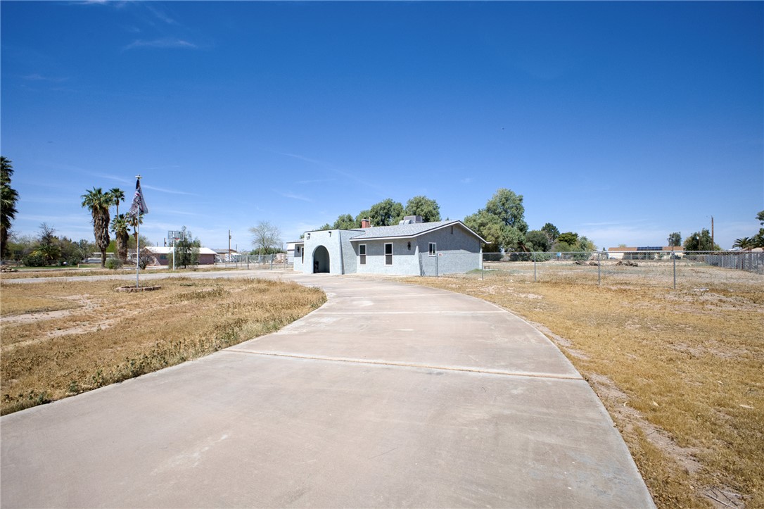 2053 Regents Road Mohave Valley, AZ 86440 - Photo 53 of 65 Exterior view of the property featuring a light blue stucco finish, a paved driveway, and a chain-link fence