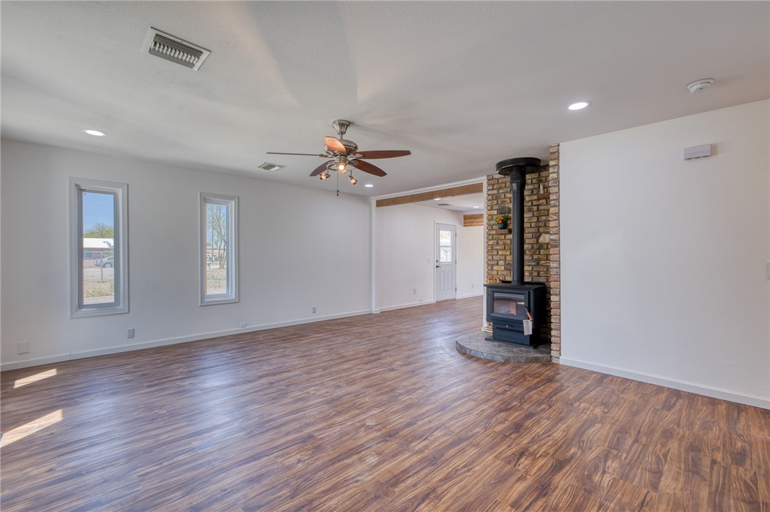 2053 Regents Road Mohave Valley, AZ 86440 - Photo 5 of 65 Spacious interior featuring wood-look flooring, multiple windows, a ceiling fan, and a stone-clad wood-burning stove with a hearth