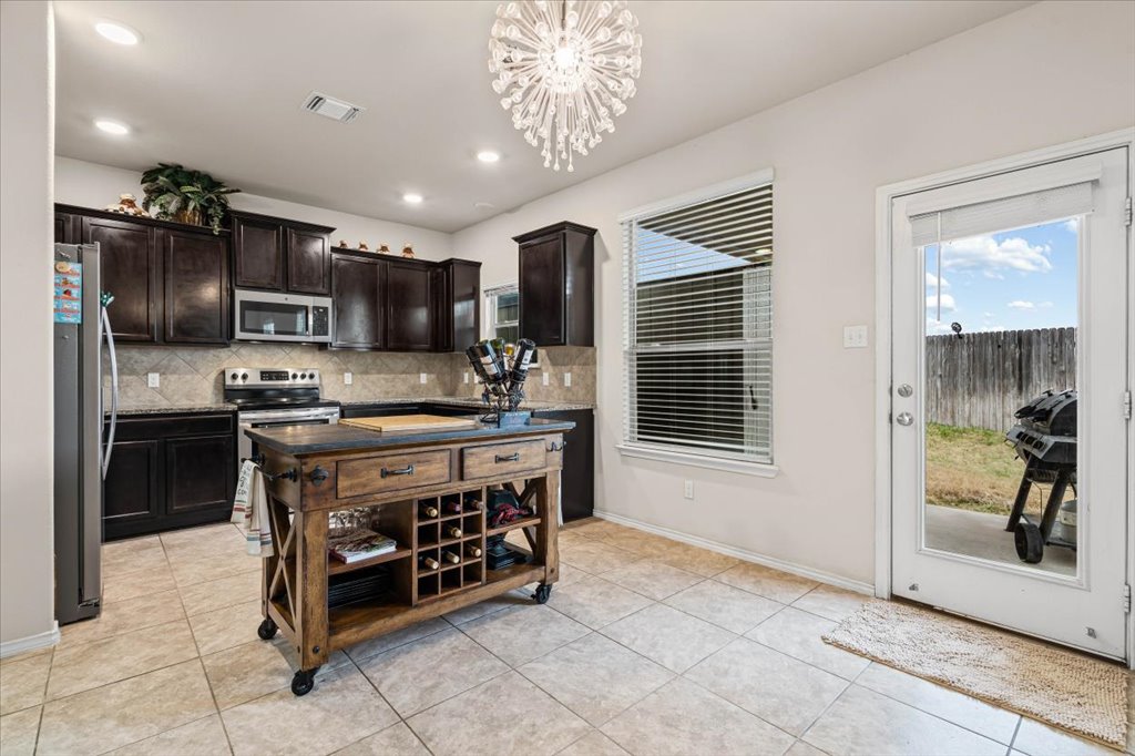 212 Plata Lane Jarrell, TX 76537 - Photo 10 of 30 Kitchen with dark wood finish cabinets, dark stone countertops, plenty of natural light, and stainless steel appliances