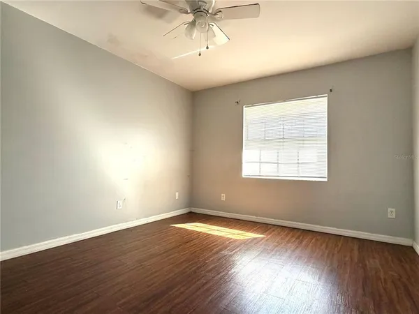 an empty room with wooden floor chandelier fan and windows