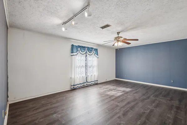 a view of an empty room with wooden floor and a ceiling fan