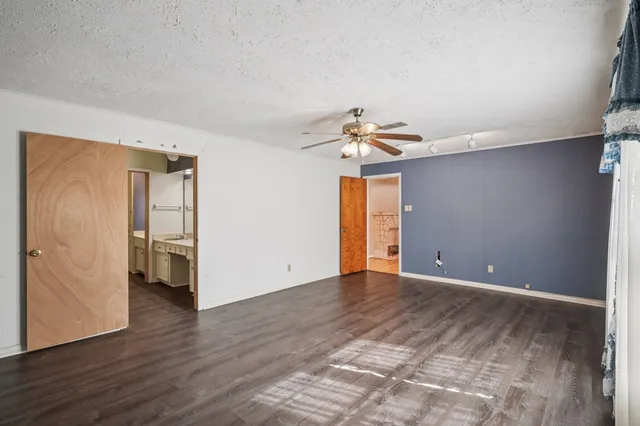 a view of an empty room with wooden floor and a ceiling fan
