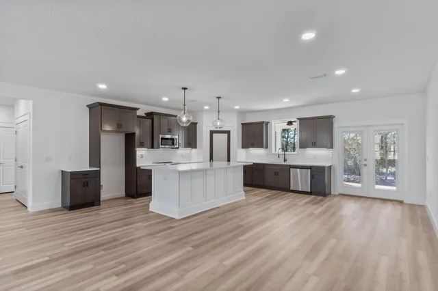 a large white kitchen with stainless steel appliances kitchen island a stove a refrigerator a oven and a large countertops with wooden floor