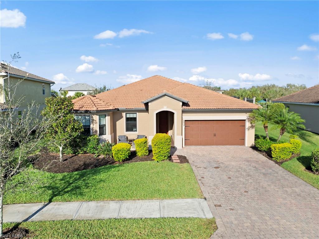 Mediterranean / spanish home featuring an attached garage, stucco siding, decorative driveway, a front lawn, and a tiled roof