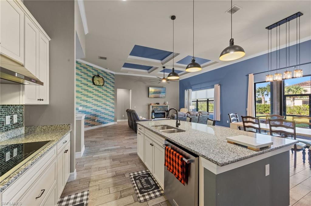 4914 Seton Way Immokalee, FL 34142 - Photo 11 of 46 Kitchen featuring coffered ceiling, light stone counters, white cabinetry, dishwasher, and an island with sink