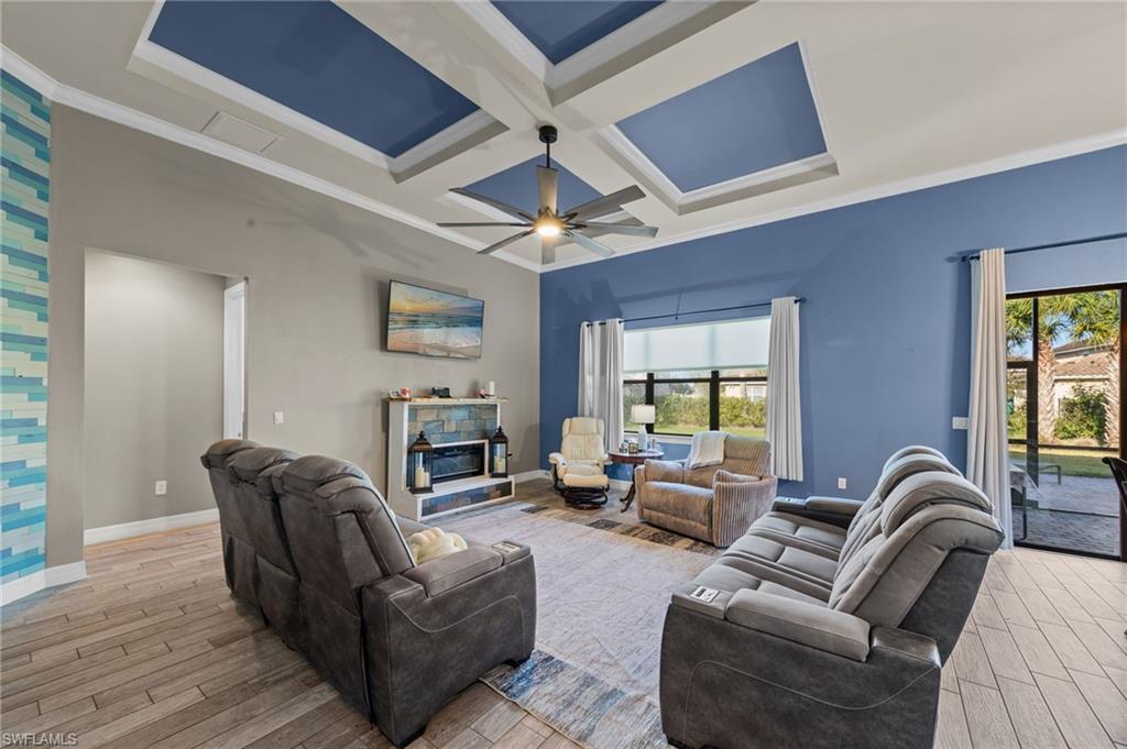 4914 Seton Way Immokalee, FL 34142 - Photo 14 of 46 Living room featuring coffered ceiling, light wood-style floors, a stone fireplace, ornamental molding, and ceiling fan