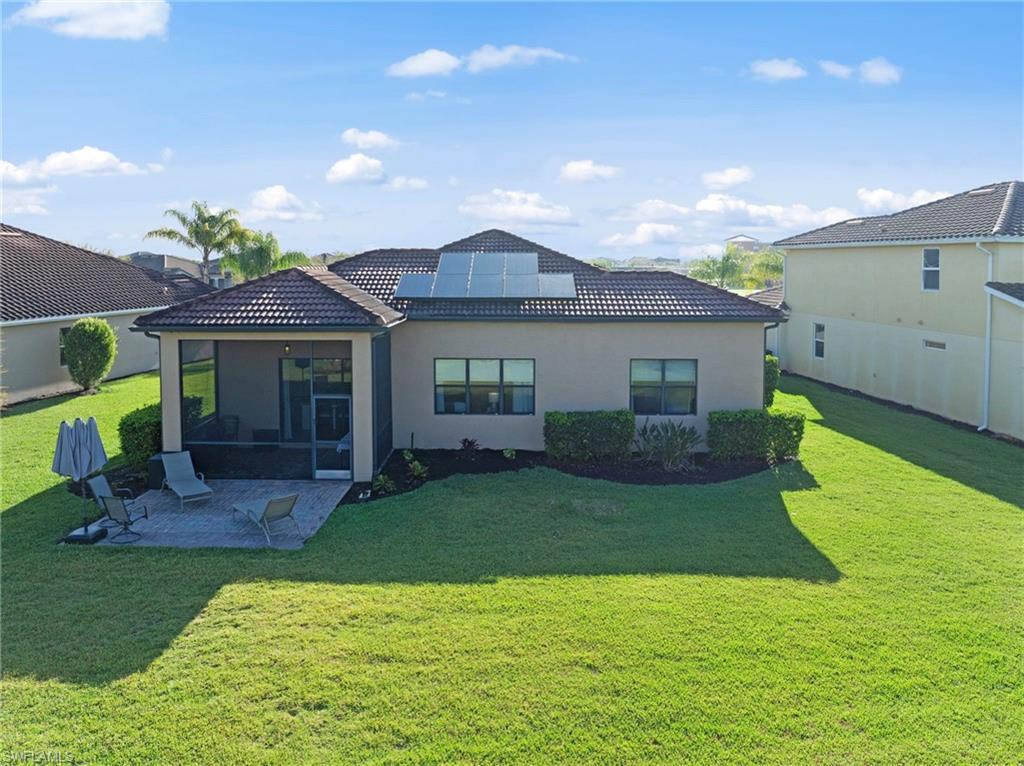 4914 Seton Way Immokalee, FL 34142 - Photo 41 of 46 Back of house with roof mounted solar panels, a yard, a sunroom, stucco siding, and a tile roof
