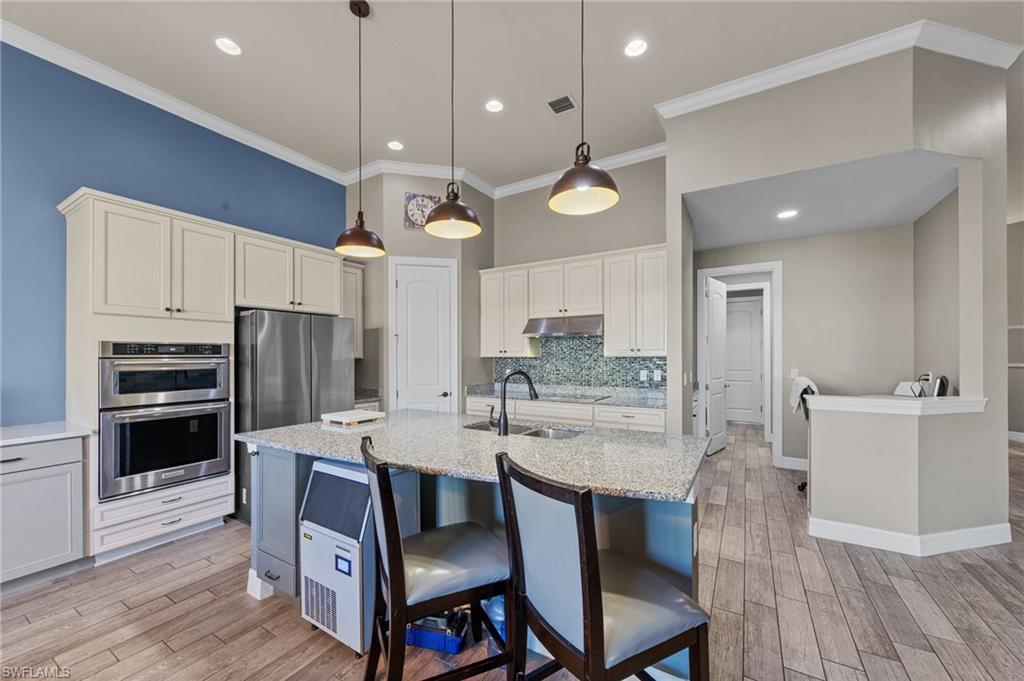 4914 Seton Way Immokalee, FL 34142 - Photo 7 of 46 Kitchen featuring light stone countertops, a breakfast bar area, wood finish floors, crown molding, and backsplash
