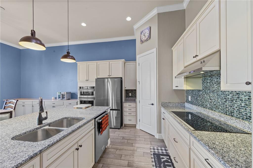4914 Seton Way Immokalee, FL 34142 - Photo 9 of 46 Kitchen featuring stainless steel appliances, crown molding, hanging light fixtures, light wood-type flooring, and light stone countertops