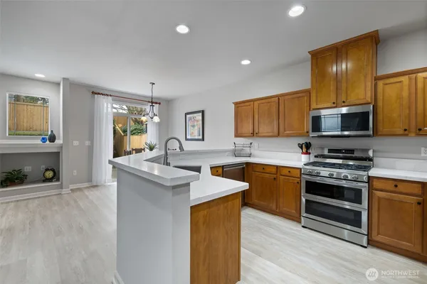 a kitchen with stainless steel appliances granite countertop a stove top oven a sink dishwasher a refrigerator and a dining table with wooden floor