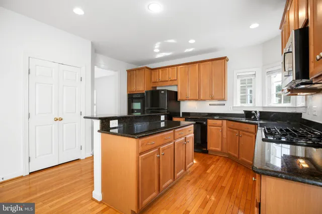 a kitchen with stainless steel appliances granite countertop wooden cabinets a refrigerator a sink a stove a microwave and wooden floors