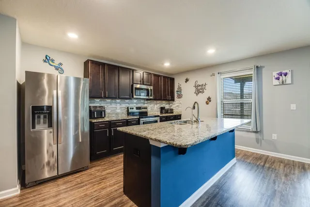 a kitchen with kitchen island granite countertop wooden cabinets a refrigerator and a stove