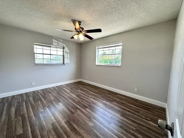 an empty room with wooden floor fan and windows