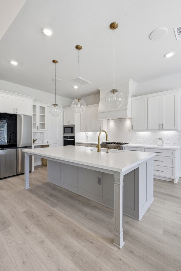 26923 Arethusa Court Spring, TX 77389 - Photo 36 of 44 This kitchen features a sleek and modern design with white cabinetry, stainless steel appliances, and a spacious island with seating. Pendant lighting adds elegance, while an adjacent dining area offers ample space for entertaining. Light wood flooring enhances the airy, contemporary feel.