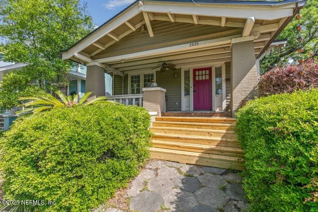 a view of a house with potted plants and a large tree