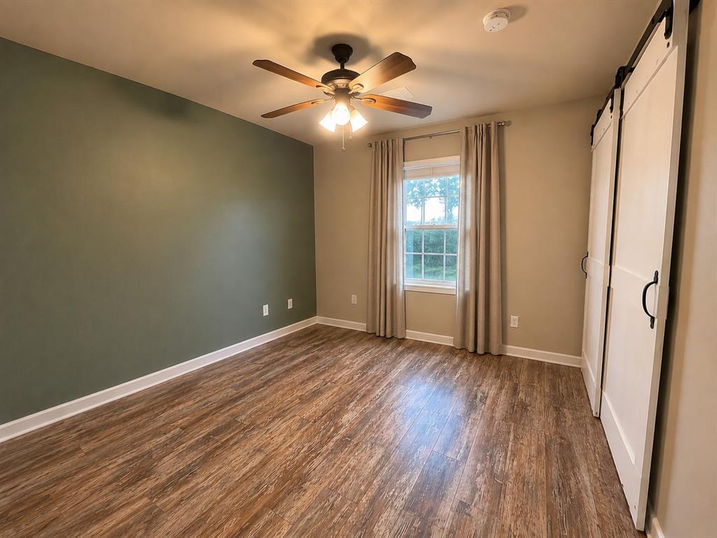 420 Sessums Road Springtown, TX 76082 - Photo 32 of 40 Spacious room featuring wood-finish flooring, a ceiling fan with integrated lighting, and a window with white trim, barn door closet