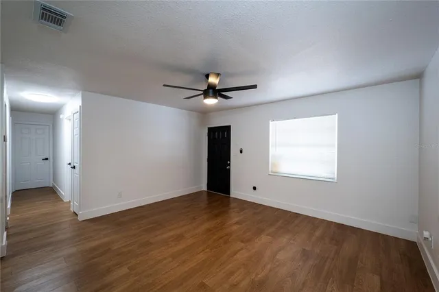 an empty room with wooden floor chandelier fan and windows