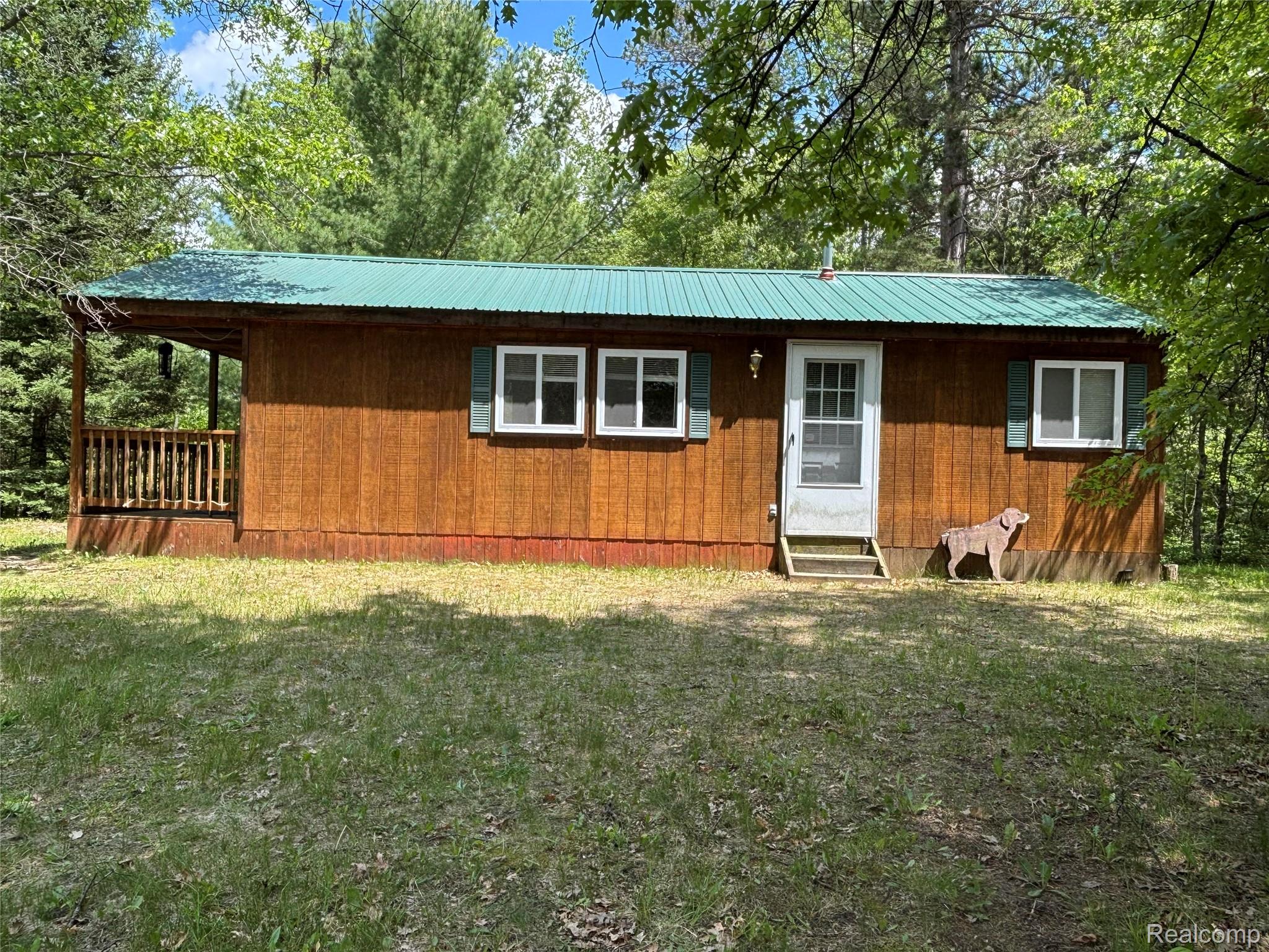 955 Aeronca Road Luzerne, MI 48636 - Photo 1 of 20 Wood-sided exterior featuring a green metal roof, white-framed windows with green shutters, and a covered porch with wooden railings
