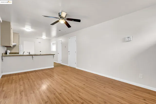 a view of an empty room with wooden floor and a ceiling fan