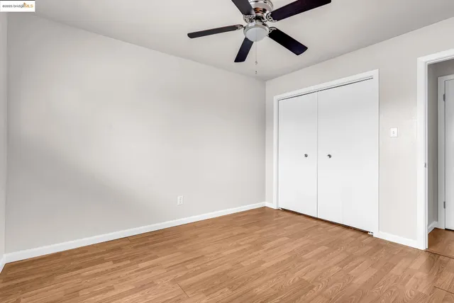 an empty room with wooden floor closet and fan