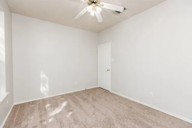 an empty room with a chandelier fan and windows