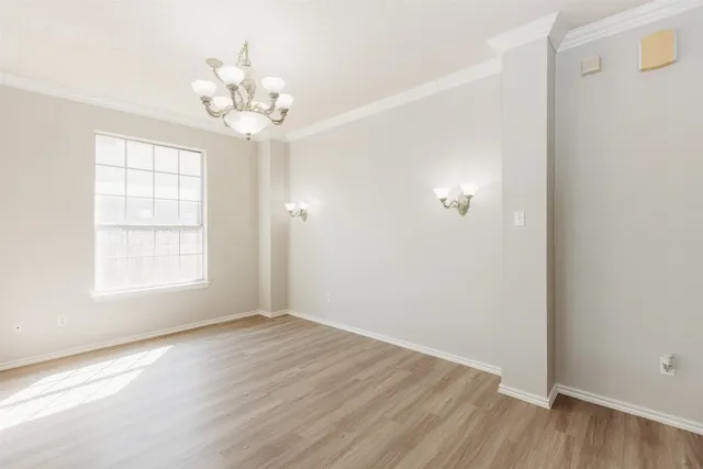 an empty room with wooden floor chandelier and windows