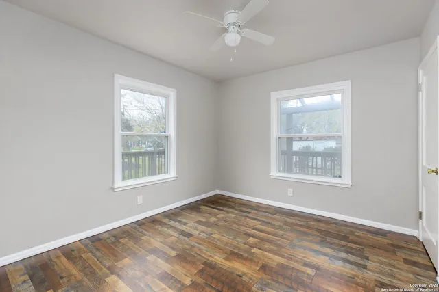 an empty room with wooden floor ceiling fan and windows