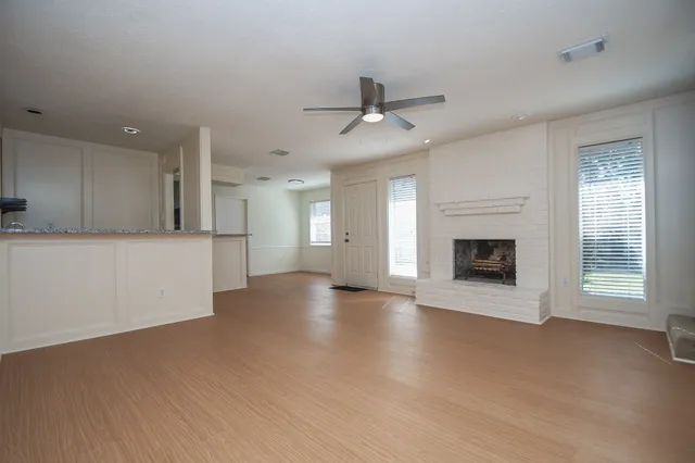 a view of a livingroom with a fireplace a ceiling fan and windows