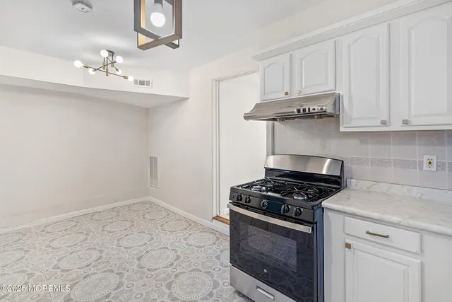 a kitchen with granite countertop a stove a sink dishwasher and white cabinets with wooden floor