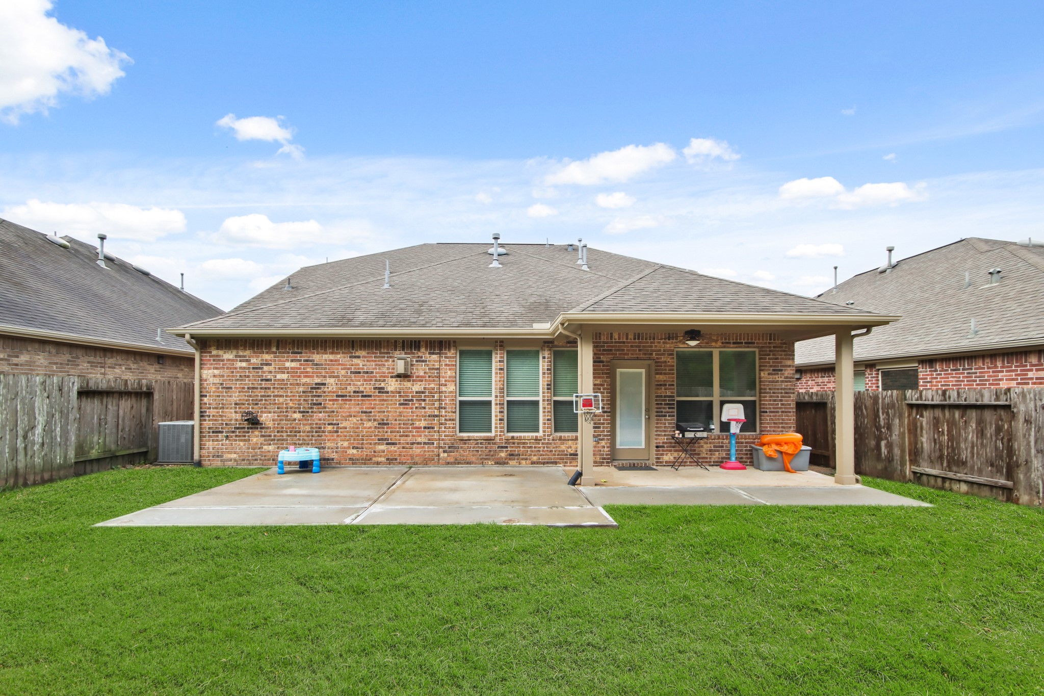 23122 Biddle Drive Porter, TX 77365 - Photo 20 of 26 Spacious backyard featuring an extended concrete patio, perfect for outdoor seating, decor, or a barbecue setup. A covered porch right outside the back door provides shade and protection, creating an ideal space for relaxation and entertaining.