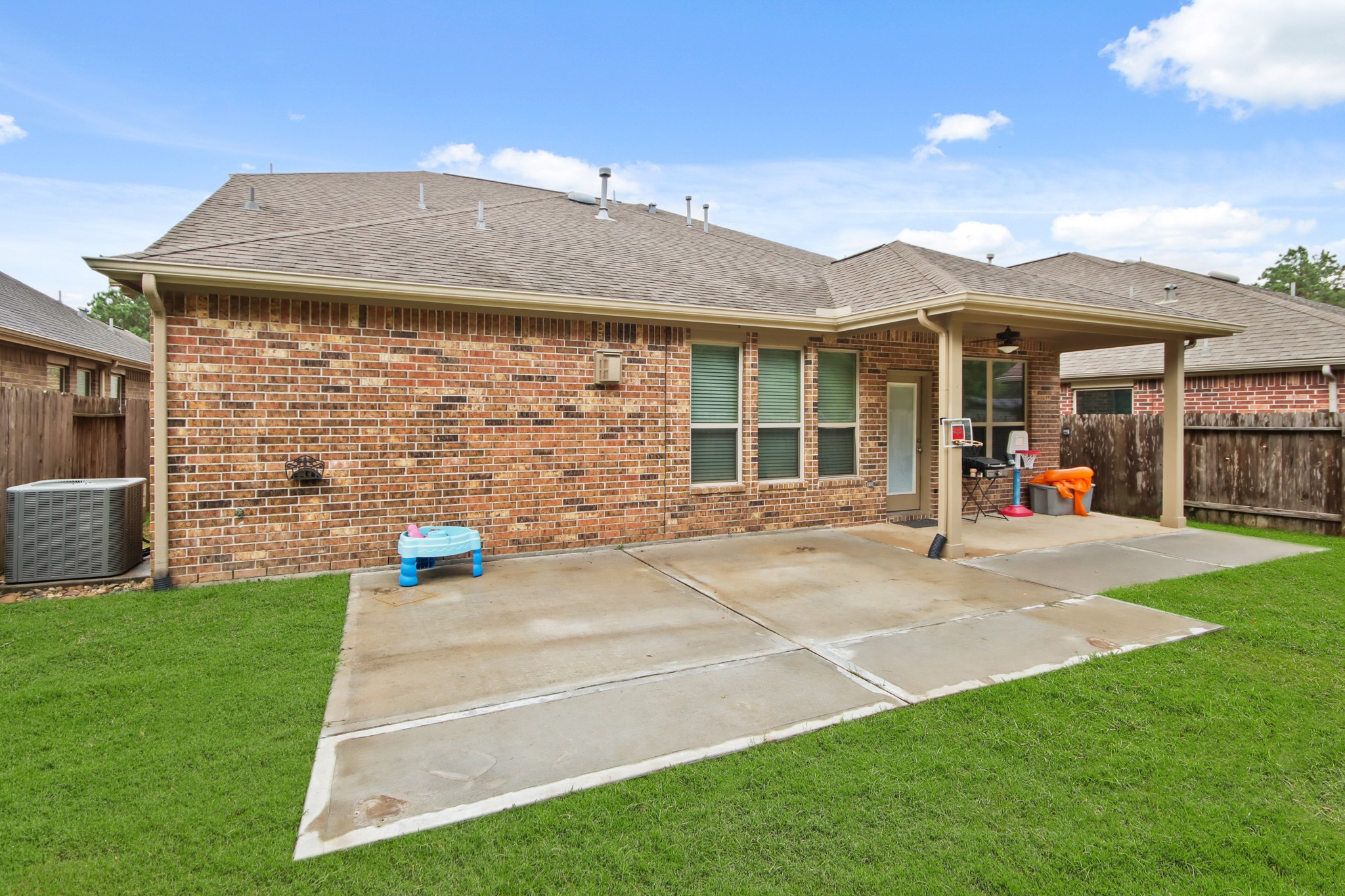23122 Biddle Drive Porter, TX 77365 - Photo 21 of 26 Spacious backyard featuring an extended concrete patio, perfect for outdoor seating, decor, or a barbecue setup. A covered porch right outside the back door provides shade and protection, creating an ideal space for relaxation and entertaining.