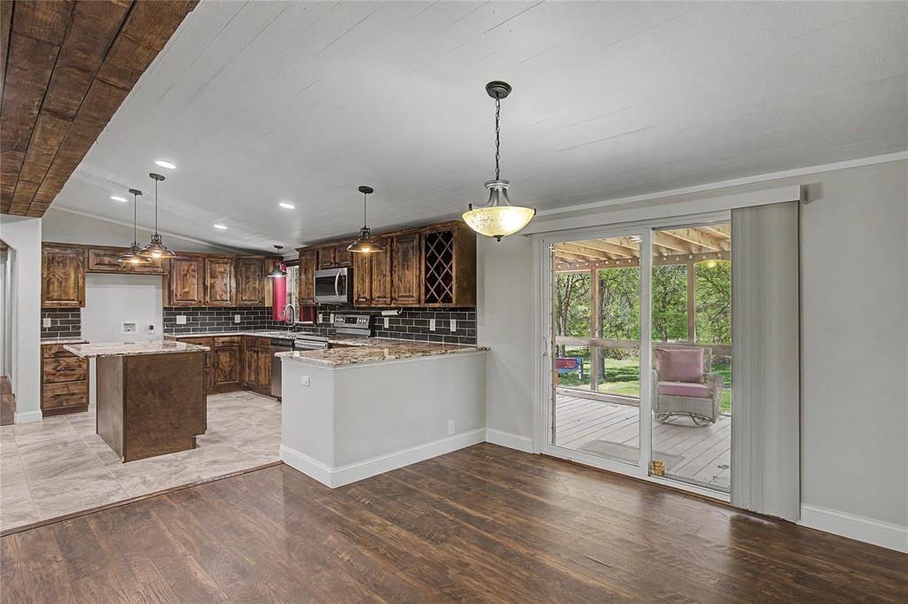 1701 Central Road Weatherford, TX 76088 - Photo 16 of 40 Kitchen with a kitchen island, custom cabinetry, granite countertops, decorative subway backsplash, vaulted ceiling, and farmhouse lighting.