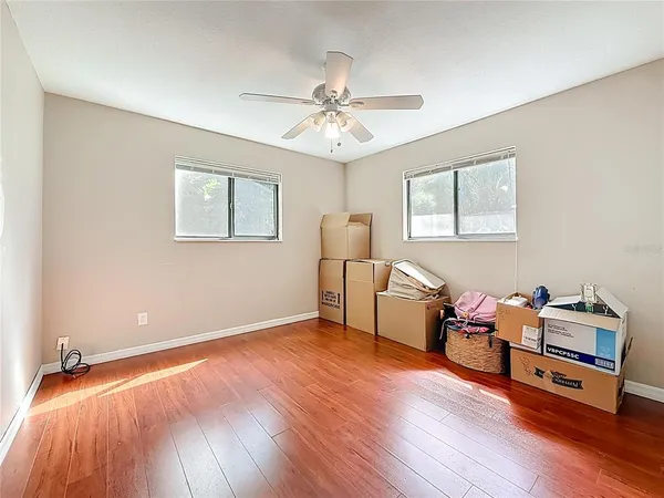 a view of an empty room with wooden floor and a ceiling fan