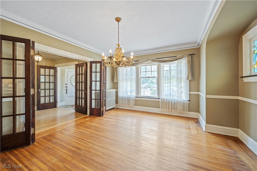 24510 Lake Road Bay Village, OH 44140 - Photo 16 of 45 Unfurnished dining area featuring french doors, light wood-style floors, crown molding, a chandelier, and radiator heating unit