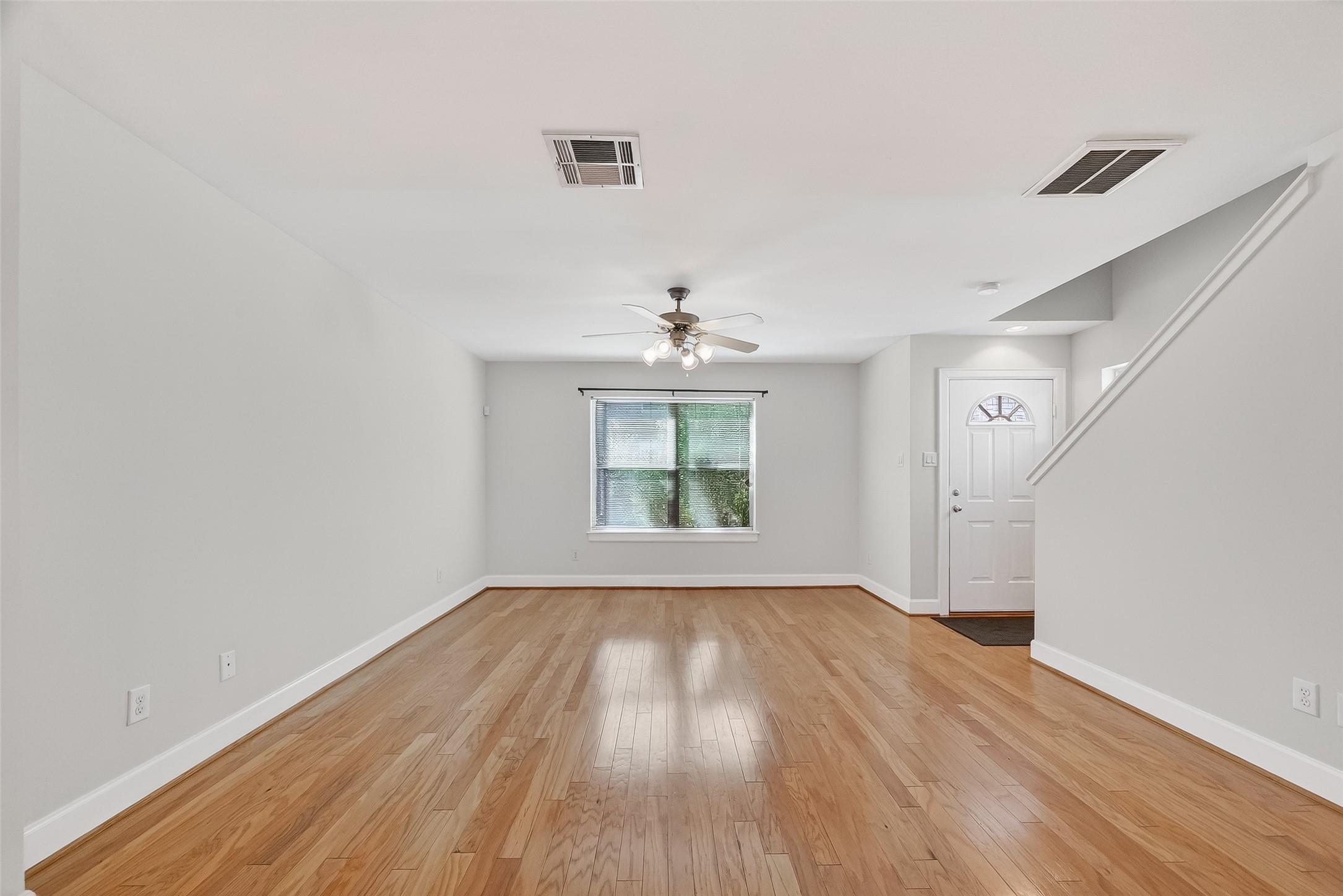 5951 S Loop East, Unit 47 Houston, TX 77033 - Photo 8 of 37 Bright and spacious living area with hardwood floors and neutral walls. Features a large window for natural light and a staircase near the entrance, creating a welcoming ambiance.