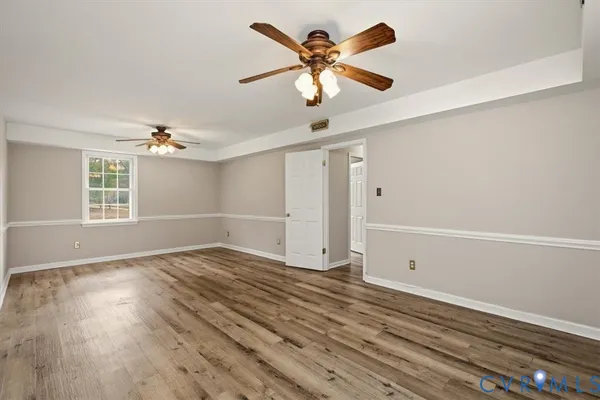 an empty room with wooden floor chandelier fan and windows