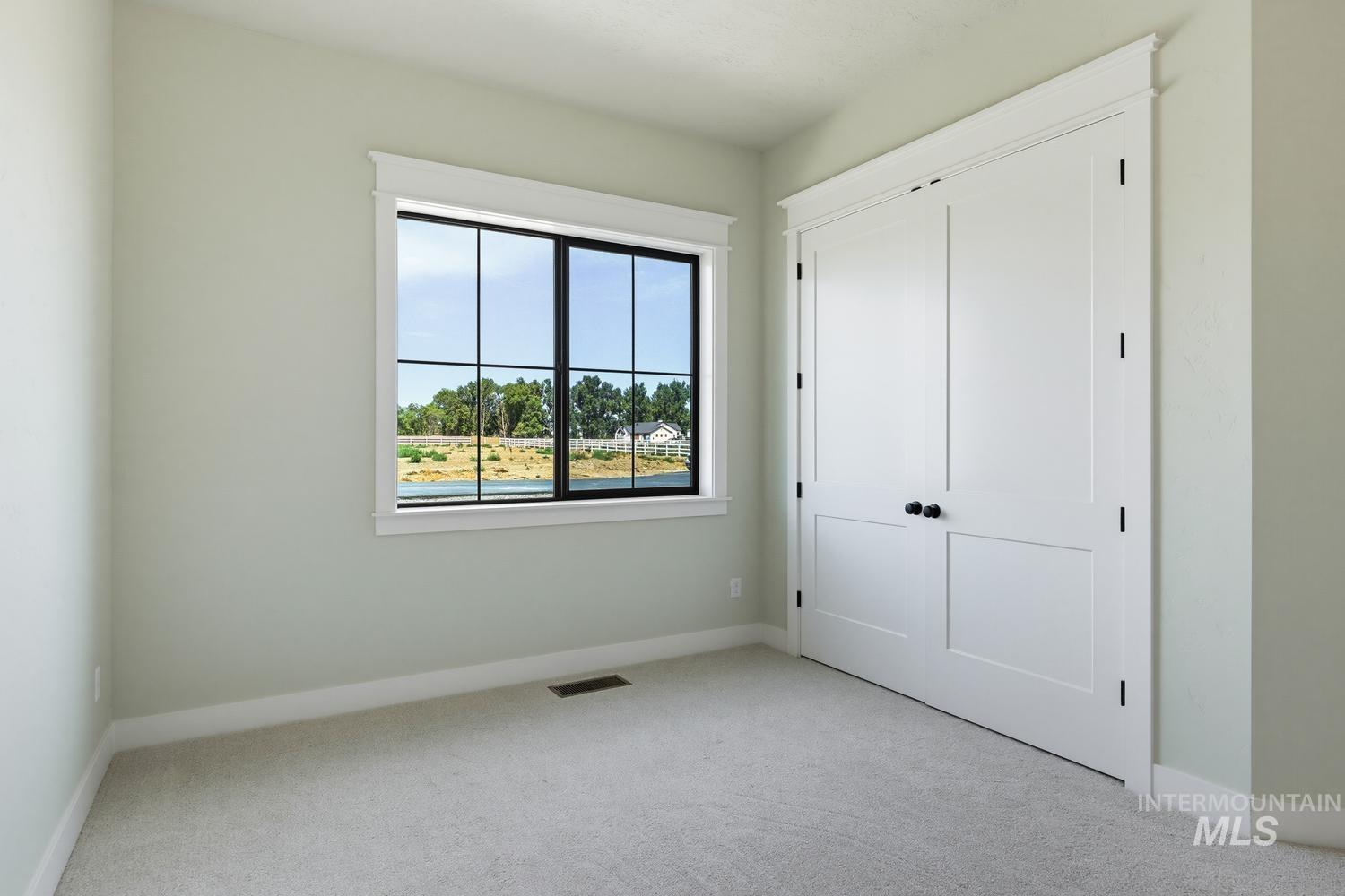 5054 Heritage Drive Marsing, ID 83639 - Photo 26 of 38 Room featuring light-toned carpeting, a large black-framed window, white trim, and a double-door closet with black hardware and decorative molding
