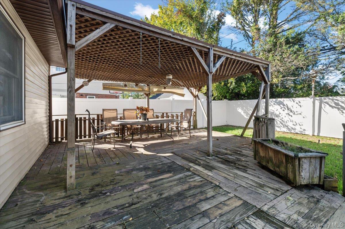 3 Surrey Lane Bethpage, NY 11714 - Photo 24 of 33 a view of a patio with table and chairs with wooden floor and fence next to a yard