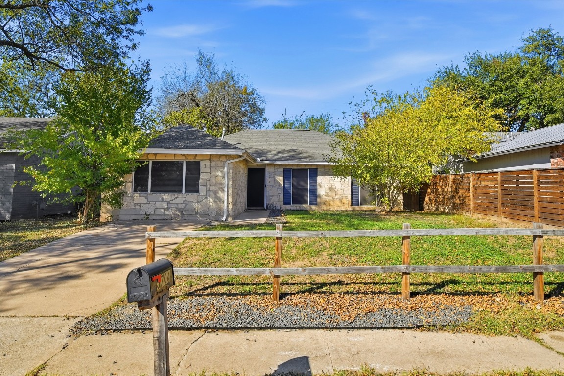 Ranch-style house featuring a fenced front yard, stone siding, and full trees