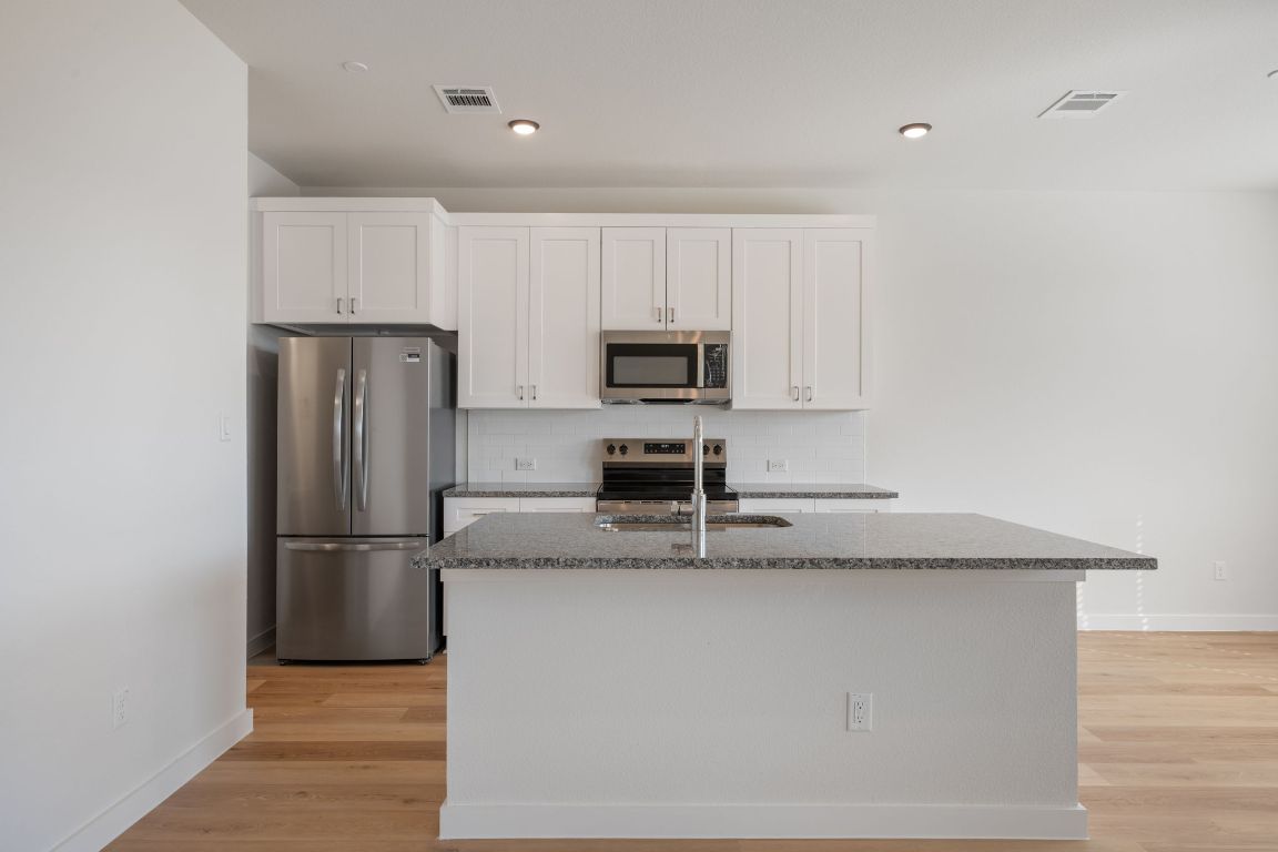 2600 Gattis School Road, Unit 1202 Round Rock, TX 78664 - Photo 6 of 24 Kitchen with decorative backsplash, stainless steel appliances, white cabinetry, dark stone countertops, and light wood-type flooring