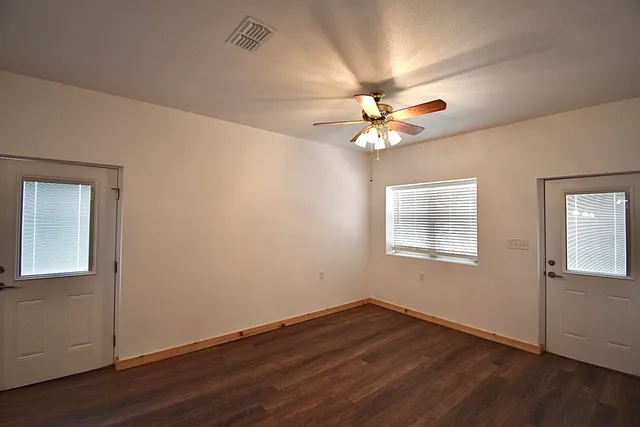 an empty room with wooden floor fan and windows