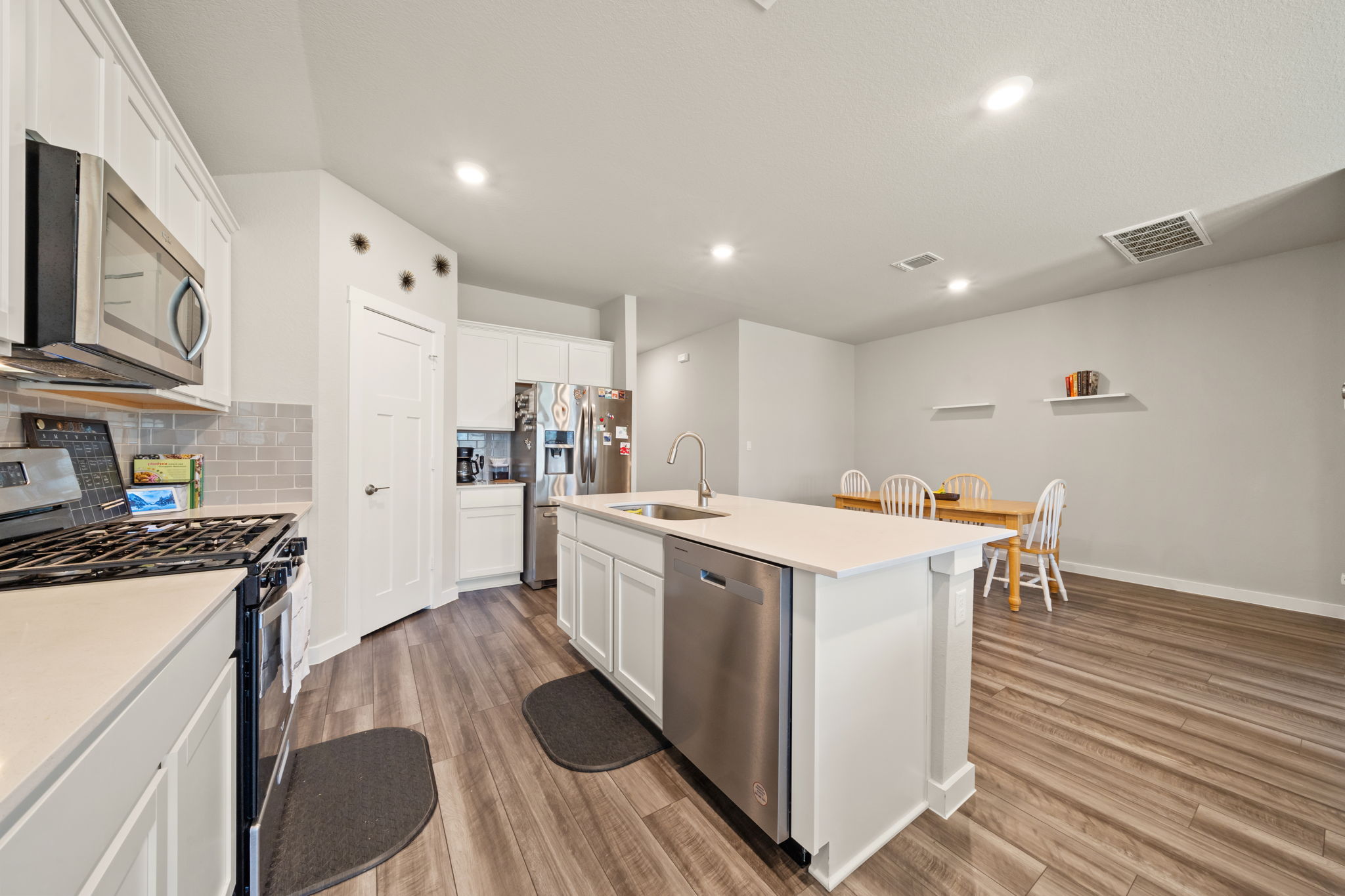 1117 Tipton Street Georgetown, TX 78633 - Photo 5 of 40 Open-concept kitchen featuring white cabinetry, light-toned countertops, stainless steel appliances, a center island with sink, and wood-finish flooring