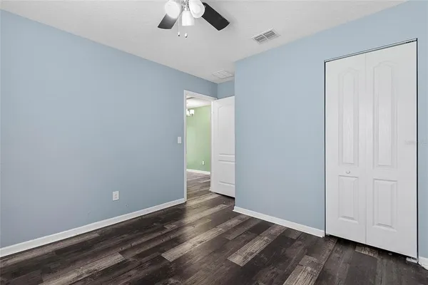 an empty room with wooden floor chandelier fan and windows