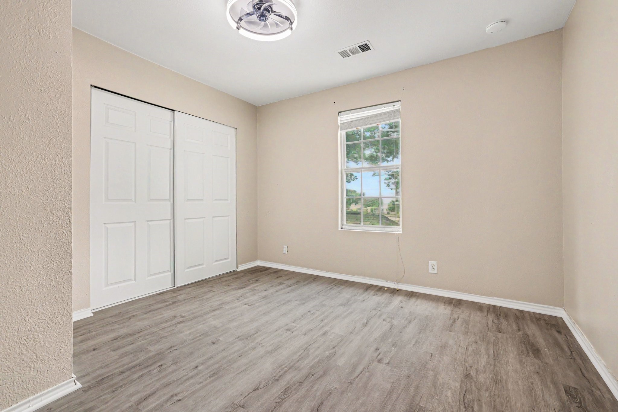 31730 Waller Tomball Road Waller, TX 77484 - Photo 36 of 50 Bright, neutral-toned bedroom with wood-look flooring, a ceiling fan, and a window providing natural light. It features a closet with sliding doors.