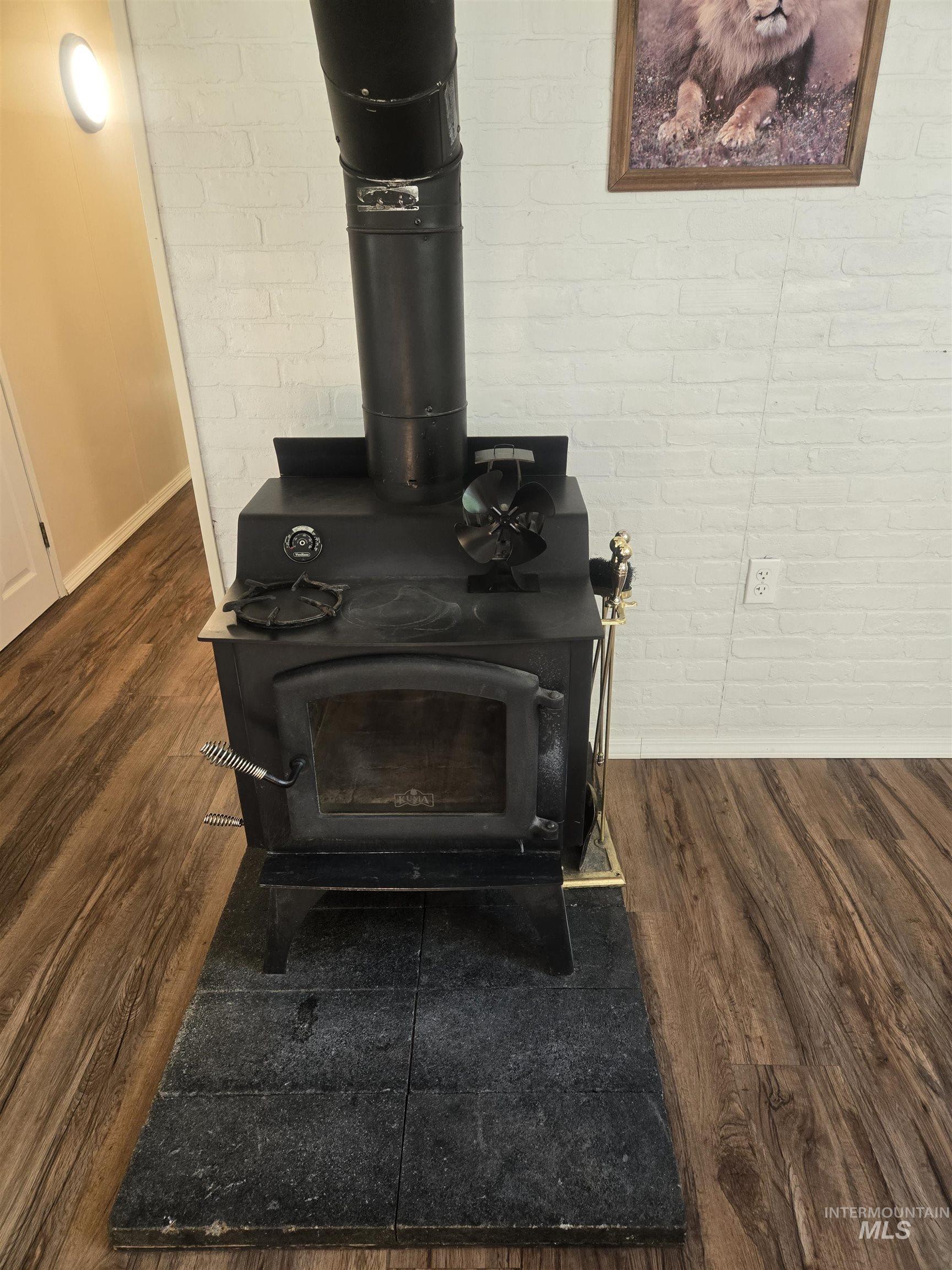 4099 Lakeview Road Orofino, ID 83544 - Photo 17 of 41 Wood-finish flooring, white brick-patterned wall, and black wood-burning stove with a stone tile hearth