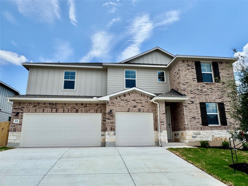 View of front facade featuring a garage, board and batten siding, driveway, and brick siding